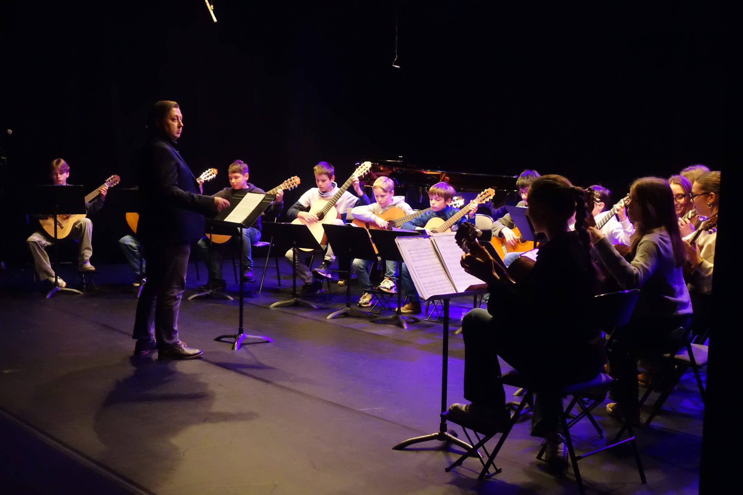 Une dizaine d'élèves guitaristes en arc de cercle autour de leur professeur qui les dirige.